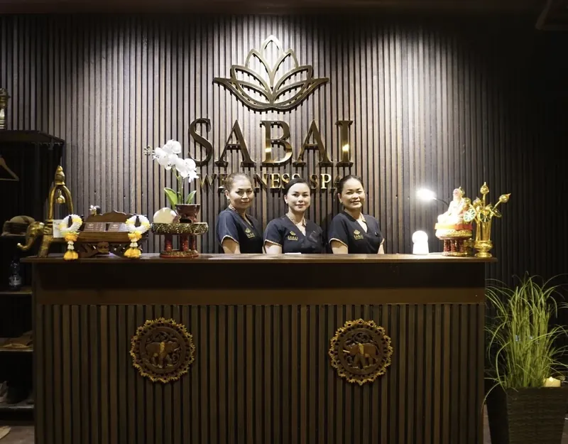 Kolme Sabain työntekijää vastaanottotiskin takana SABAI WELLNESS SPA -logon alla