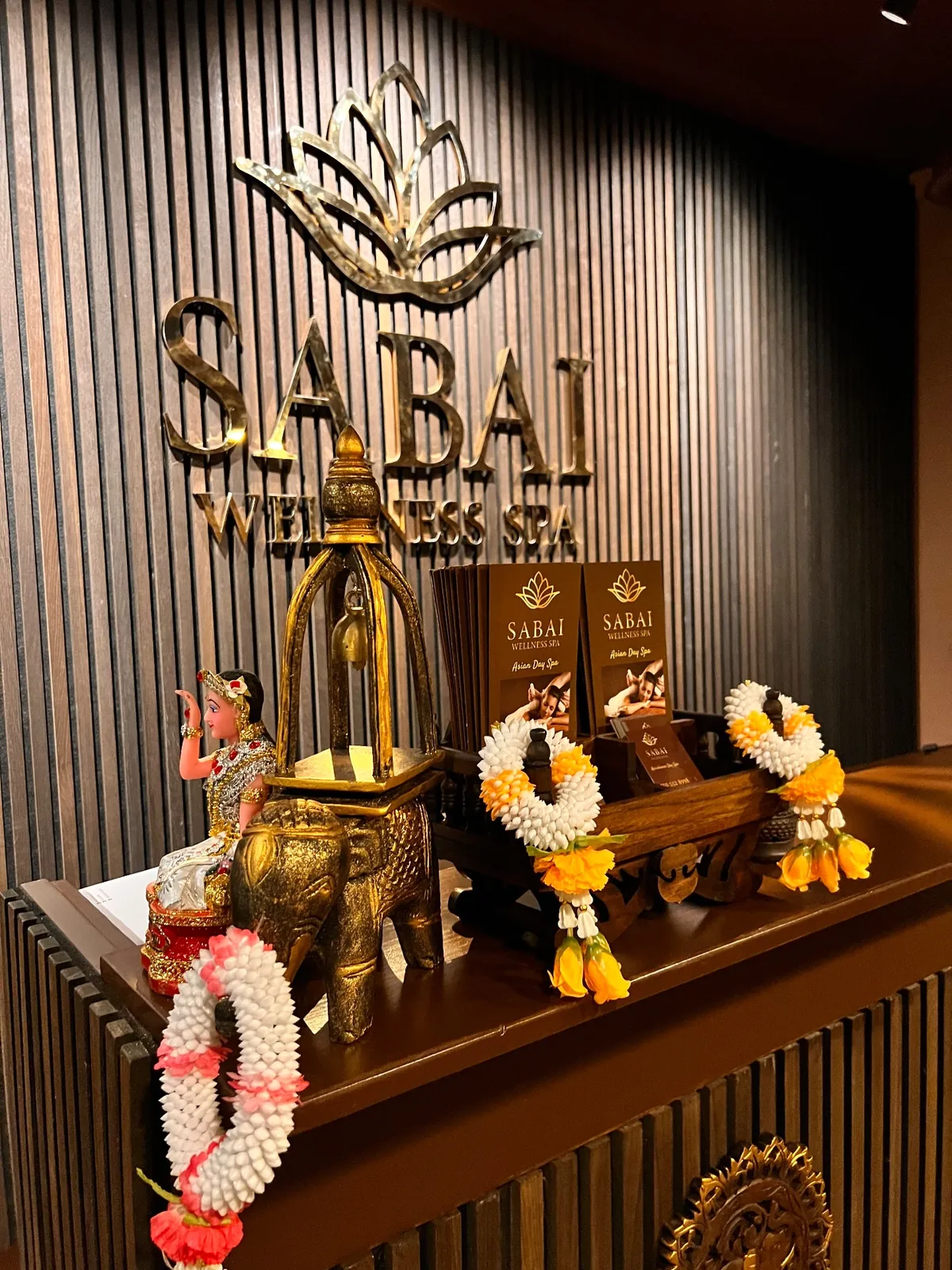 Vastaanoton alttari: kultainen norsupatsas, kukkaseppeleet ja SABAI-logo raidoitetulla seinällä